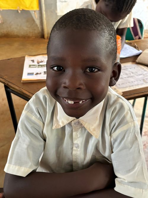 A young Wide Horizons student smiling at his classroom desk