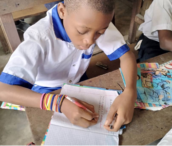 A young La Tendresse student concentrating as he writes in his notebook